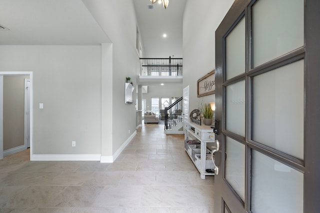 entrance foyer with stairs, visible vents, baseboards, and a towering ceiling