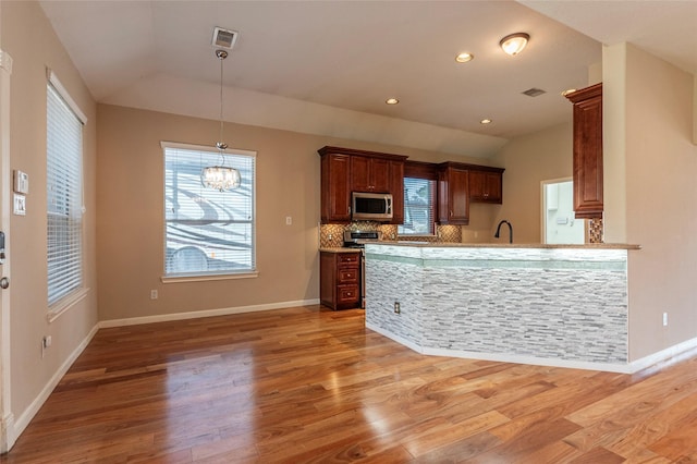 kitchen featuring a peninsula, vaulted ceiling, appliances with stainless steel finishes, decorative backsplash, and light wood finished floors