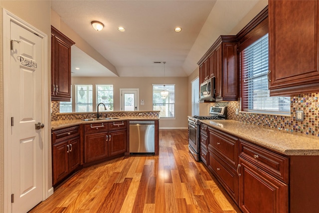 kitchen featuring light wood finished floors, stainless steel appliances, tasteful backsplash, a sink, and a peninsula