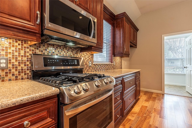 kitchen featuring stainless steel appliances, baseboards, vaulted ceiling, light wood-style floors, and backsplash