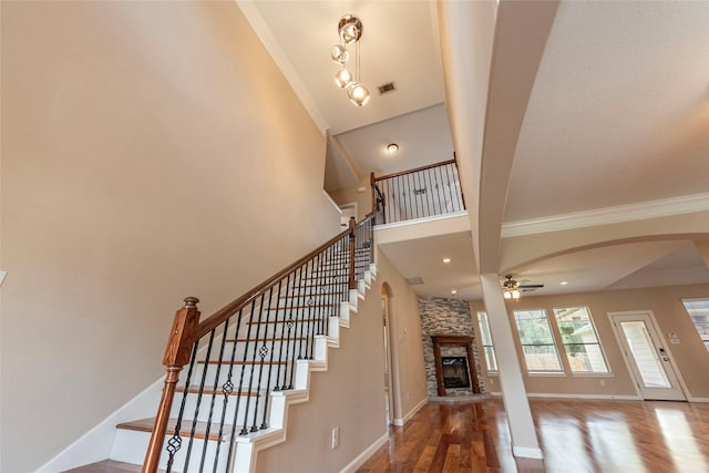 stairway with arched walkways, ornamental molding, a stone fireplace, wood finished floors, and baseboards