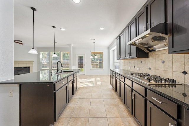 kitchen with tasteful backsplash, under cabinet range hood, stainless steel gas cooktop, a sink, and light tile patterned flooring