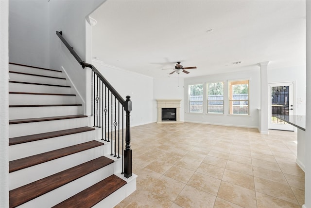 unfurnished living room with light tile patterned floors, a ceiling fan, baseboards, stairs, and a glass covered fireplace