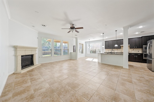 unfurnished living room with crown molding, light tile patterned floors, visible vents, a ceiling fan, and a healthy amount of sunlight