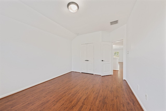 spare room with vaulted ceiling, wood finished floors, visible vents, and baseboards