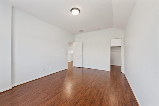 unfurnished bedroom with dark wood-type flooring, baseboards, vaulted ceiling, a closet, and a walk in closet