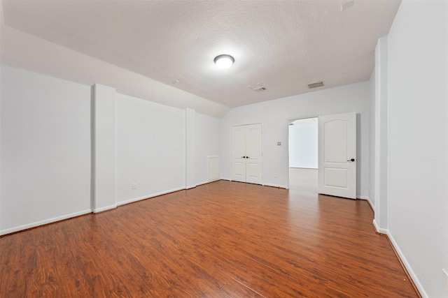 unfurnished room with a textured ceiling, wood finished floors, visible vents, and baseboards