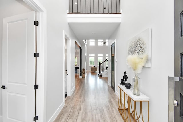 hall with light wood finished floors, baseboards, a high ceiling, and stairway