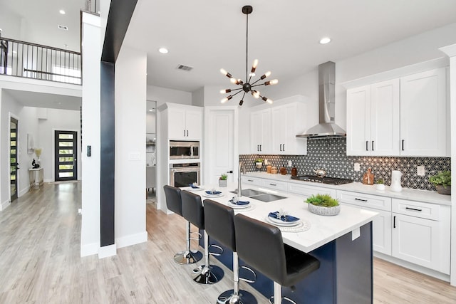 kitchen with visible vents, decorative backsplash, wall chimney exhaust hood, stainless steel appliances, and a sink