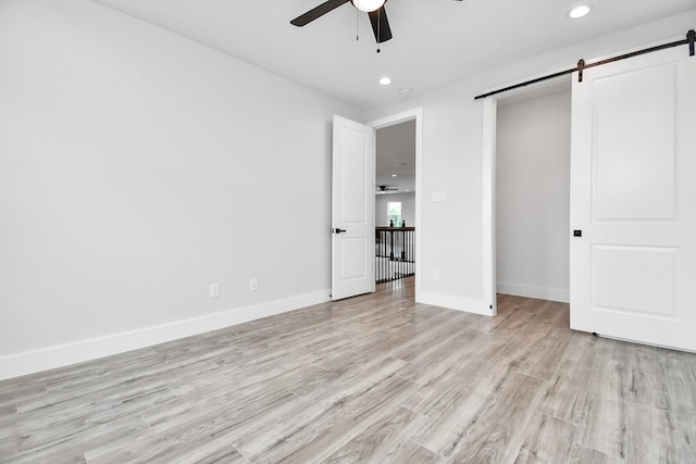 unfurnished bedroom featuring light wood-style floors, recessed lighting, baseboards, and a barn door