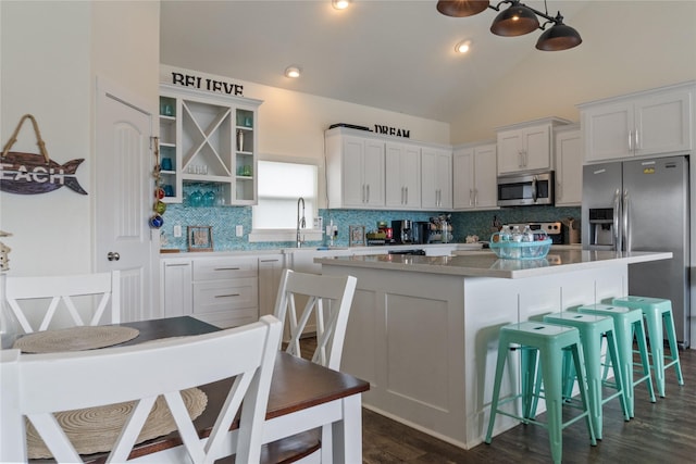 kitchen featuring a breakfast bar, a center island, stainless steel appliances, white cabinetry, and backsplash