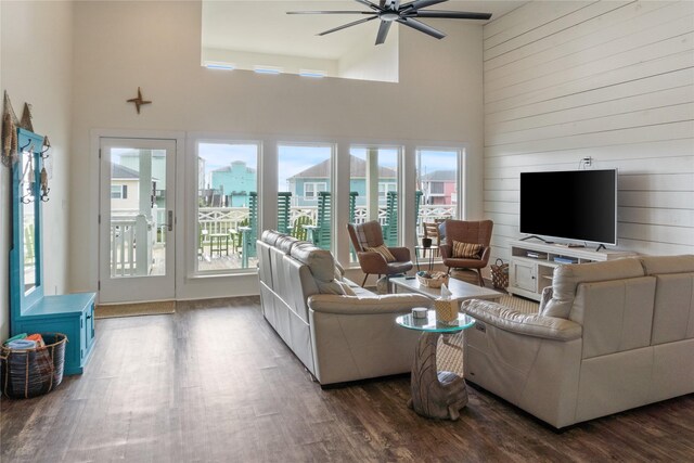 living room featuring a high ceiling, wood finished floors, a ceiling fan, and wooden walls