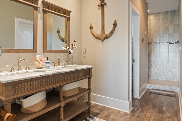 bathroom with a tile shower, wood finished floors, a sink, and baseboards