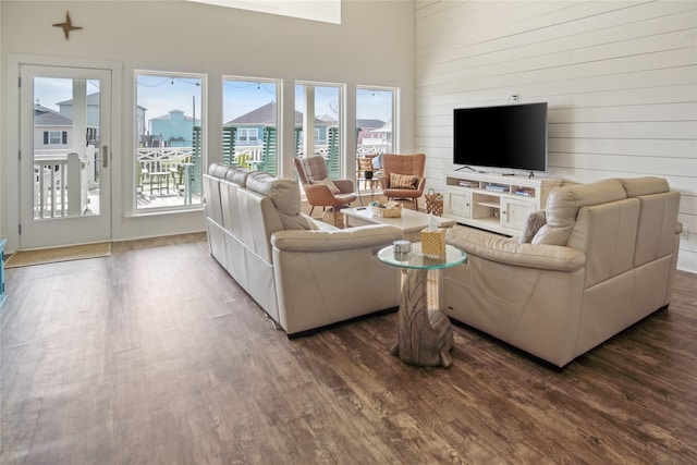 living room featuring wood walls, dark wood-style flooring, and a towering ceiling