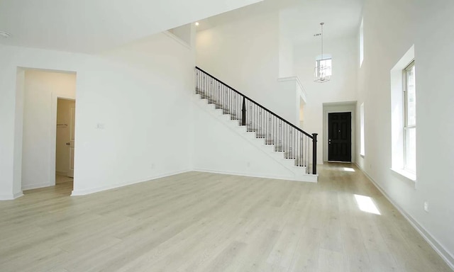 interior space featuring light wood-type flooring, baseboards, a high ceiling, and stairs