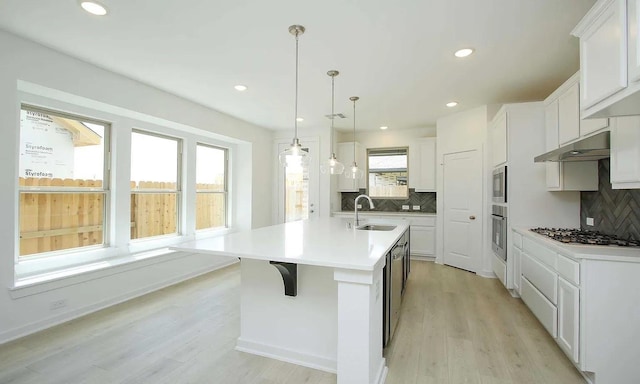 kitchen featuring appliances with stainless steel finishes, white cabinets, a kitchen island with sink, a sink, and under cabinet range hood