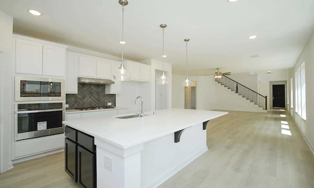 kitchen with a sink, gas cooktop, built in microwave, oven, and under cabinet range hood