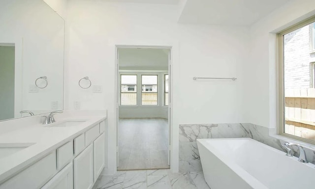 bathroom featuring marble finish floor, double vanity, a soaking tub, wainscoting, and a sink