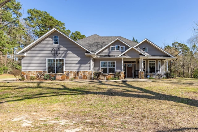 craftsman house featuring stone siding, a front lawn, covered porch, and roof with shingles