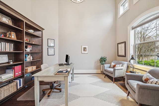 office featuring wood finished floors, a towering ceiling, and baseboards