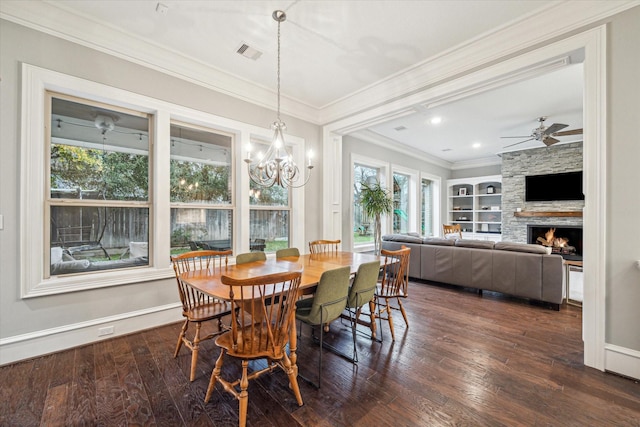 dining room featuring built in shelves, crown molding, visible vents, dark wood-type flooring, and a stone fireplace