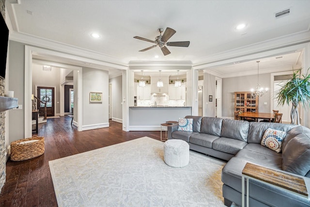 living room with dark wood finished floors, visible vents, ornamental molding, baseboards, and ceiling fan with notable chandelier