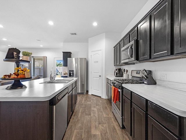 kitchen with appliances with stainless steel finishes, wood finished floors, light countertops, a sink, and recessed lighting