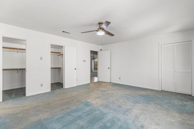 unfurnished bedroom featuring multiple closets, carpet flooring, visible vents, and baseboards