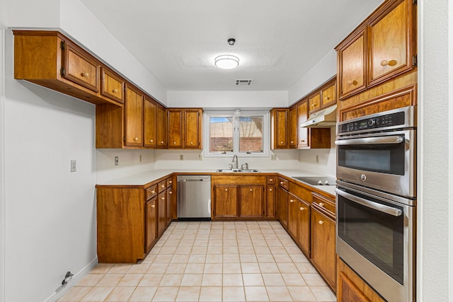 kitchen featuring under cabinet range hood, a sink, visible vents, appliances with stainless steel finishes, and brown cabinetry