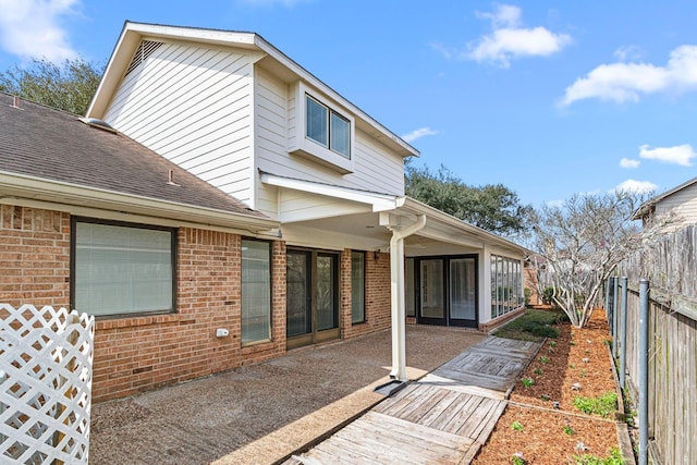 rear view of property with roof with shingles, a fenced backyard, a patio, and brick siding