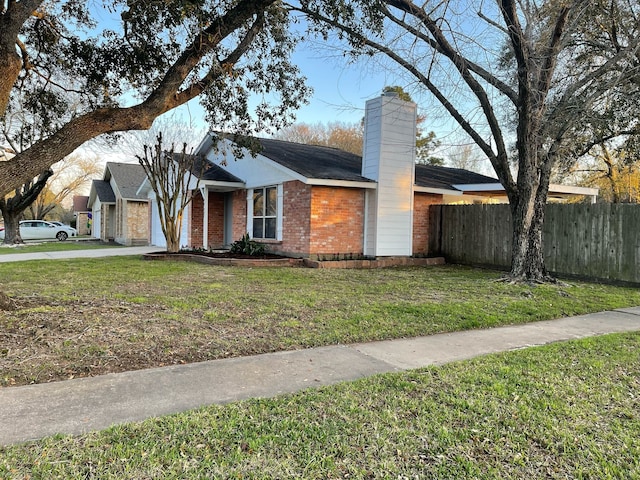 view of front facade with brick siding, a front lawn, a chimney, and fence