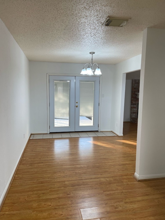 spare room featuring a chandelier, a textured ceiling, wood finished floors, visible vents, and baseboards