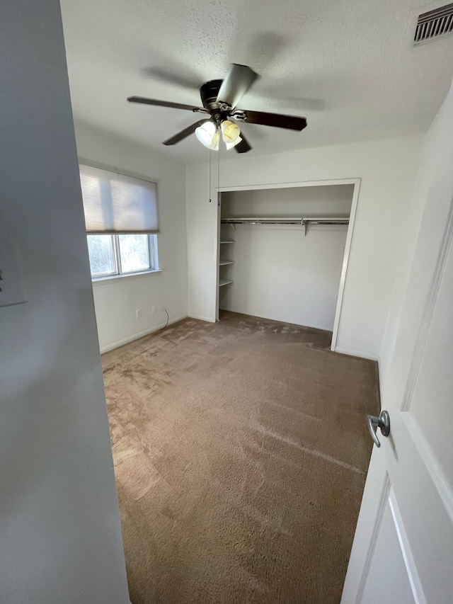 unfurnished bedroom featuring a textured ceiling, carpet flooring, visible vents, a ceiling fan, and a closet