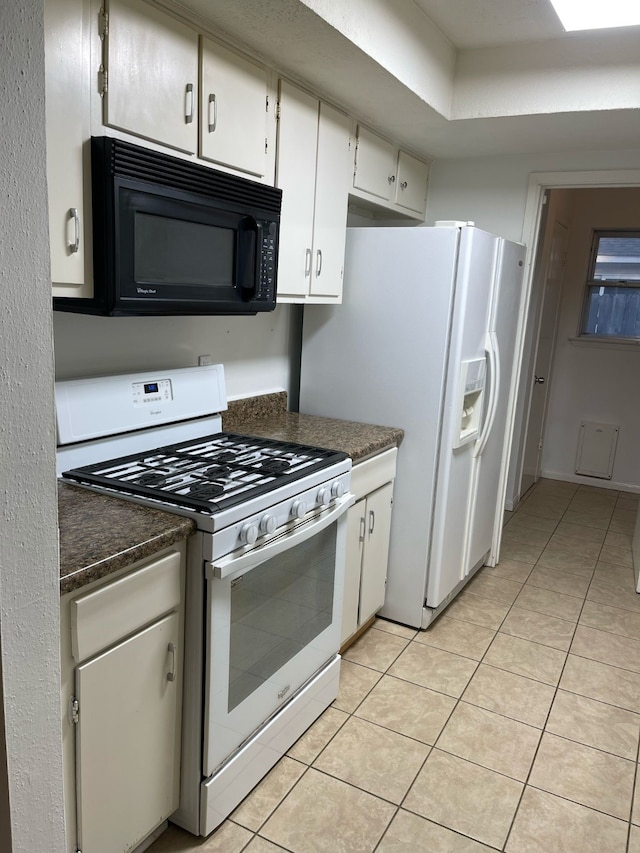 kitchen with dark countertops, white appliances, light tile patterned floors, and white cabinets