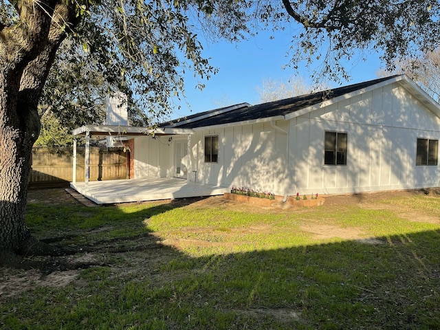 rear view of house with a lawn, a wooden deck, and fence