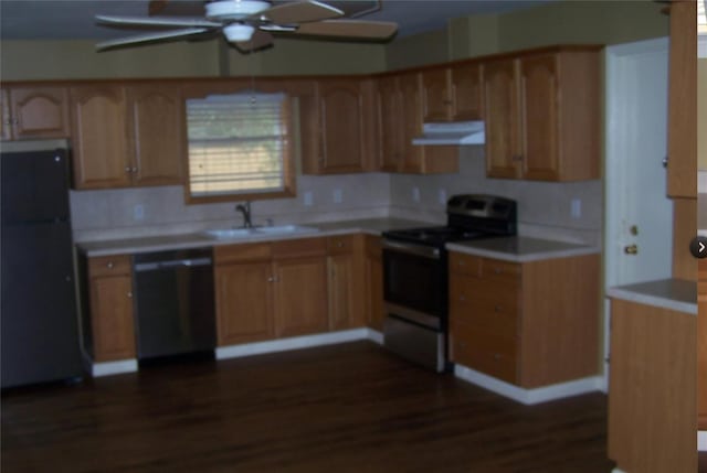 kitchen featuring under cabinet range hood, stainless steel appliances, a sink, light countertops, and dark wood finished floors