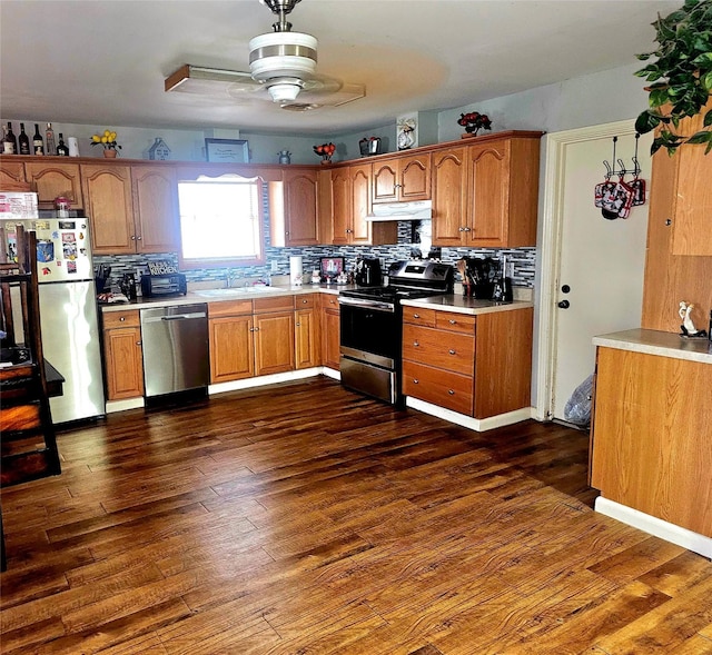 kitchen featuring dark wood-style flooring, brown cabinetry, appliances with stainless steel finishes, light countertops, and under cabinet range hood