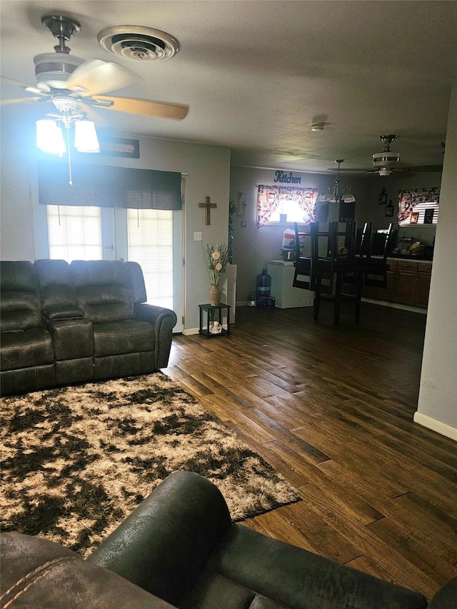 living room with wood finished floors, visible vents, baseboards, and ceiling fan