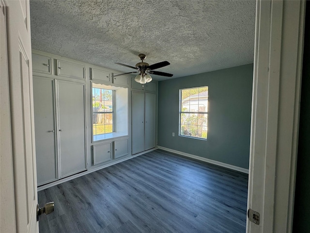 unfurnished bedroom with dark wood-style flooring, multiple windows, a textured ceiling, and baseboards