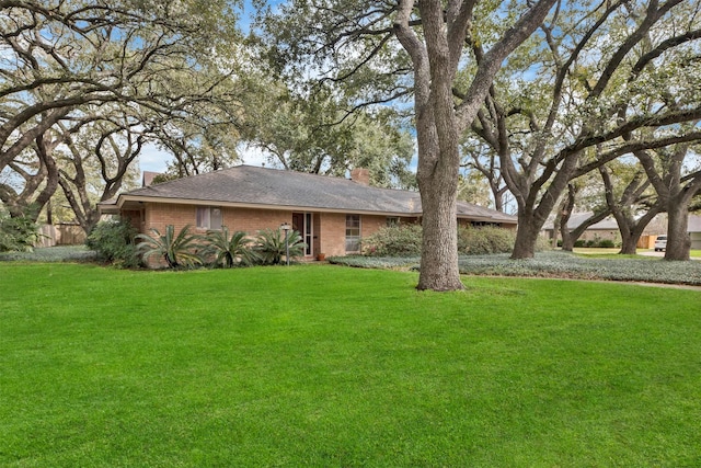 single story home featuring brick siding, a chimney, and a front yard