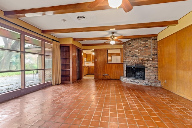 unfurnished living room with wooden walls, visible vents, ceiling fan, beamed ceiling, and a fireplace