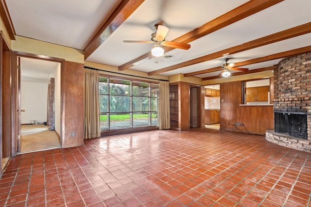 unfurnished living room with beamed ceiling, a fireplace, wood walls, and ceiling fan