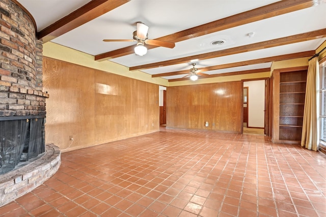 unfurnished living room featuring visible vents, beamed ceiling, a ceiling fan, wood walls, and a fireplace