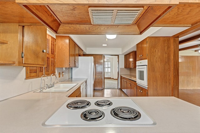 kitchen with visible vents, light countertops, brown cabinetry, white appliances, and a sink