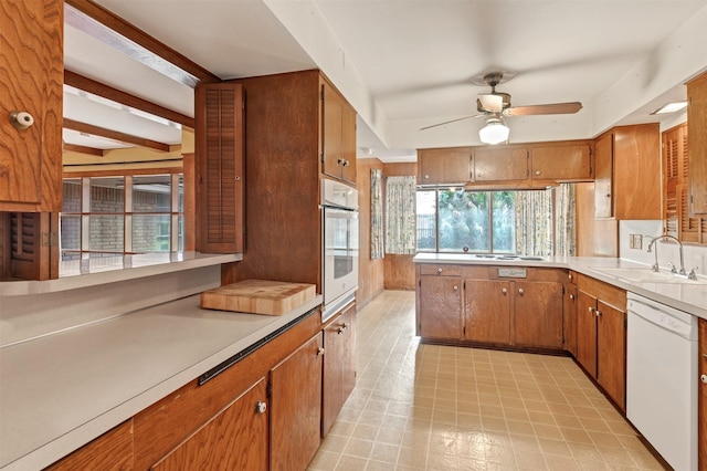 kitchen featuring white appliances, light countertops, brown cabinets, and a sink