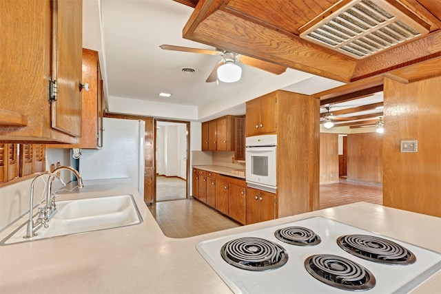 kitchen with visible vents, brown cabinets, white oven, a ceiling fan, and a sink