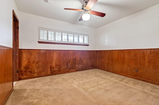 carpeted spare room featuring a ceiling fan, wood walls, and wainscoting