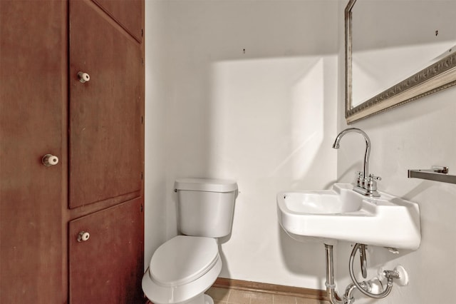 half bath featuring toilet, baseboards, and a sink