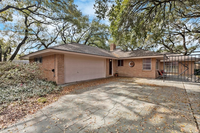 single story home featuring driveway, a shingled roof, a garage, brick siding, and a chimney