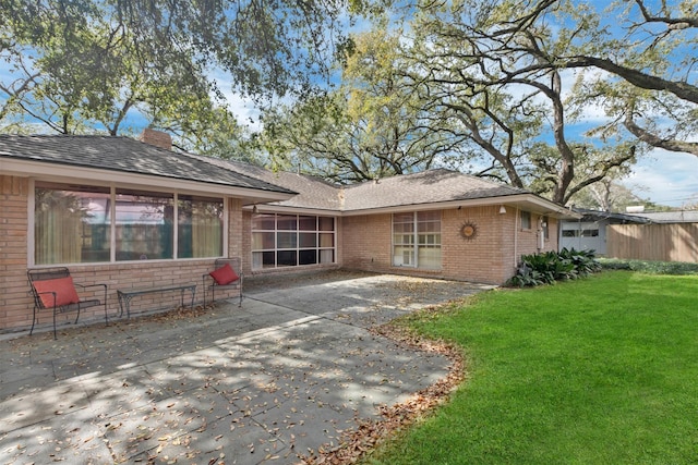 rear view of house featuring a patio, roof with shingles, a yard, a chimney, and brick siding